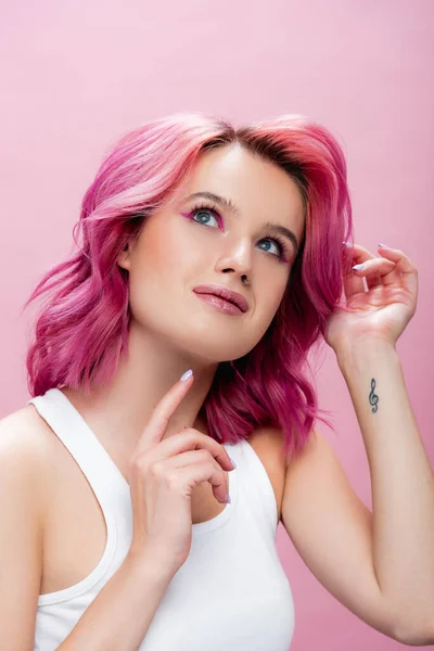Mujer joven soñadora con pelo colorido y maquillaje posando aislado en rosa - foto de stock
