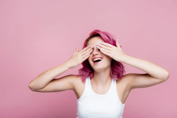 Jeune femme aux cheveux colorés souriant et couvrant les yeux avec les mains isolées sur rose — Photo de stock