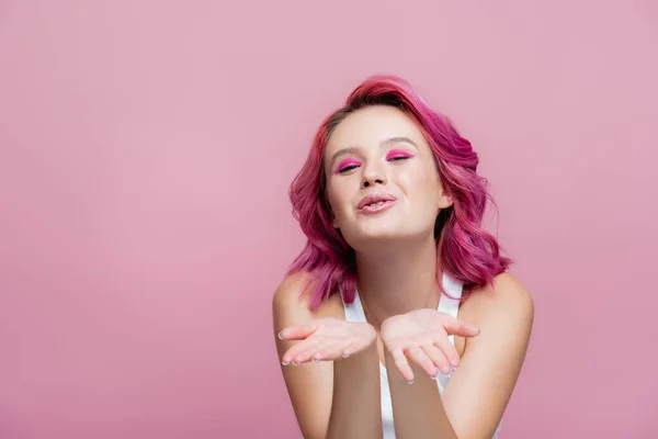 Молода жінка з барвистим волоссям, що дме поцілунок ізольовано на рожевому — стокове фото