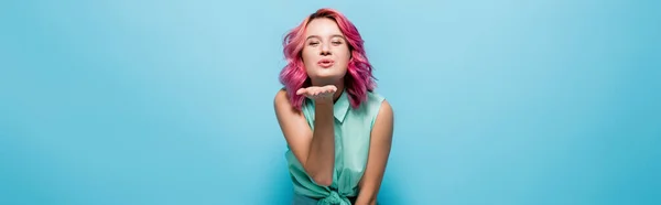 Молодая женщина с розовыми волосами дует поцелуй на голубом фоне, панорамный снимок — стоковое фото