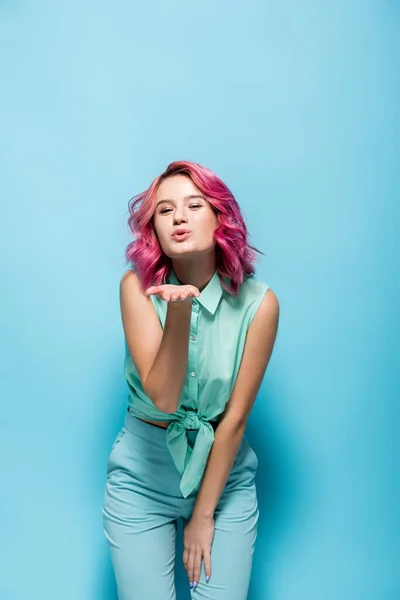 Mujer joven con pelo rosa soplando beso sobre fondo azul — Stock Photo