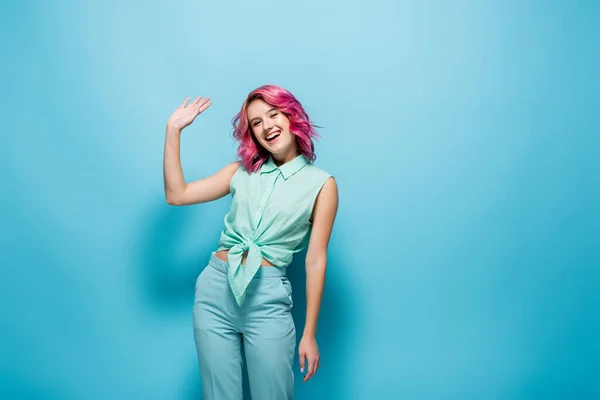 Jovem mulher com cabelo rosa acenando mão no fundo azul — Fotografia de Stock