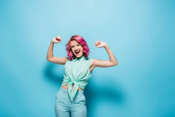 Aufgeregte junge Frau mit rosa Haaren gestikuliert auf blauem Hintergrund — Stockfoto