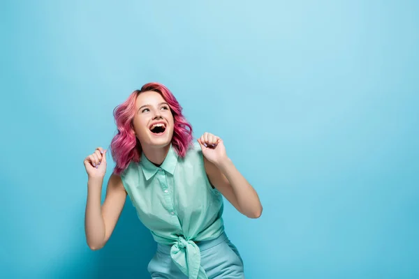 Mujer joven con pelo rosa regocijándose sobre fondo azul - foto de stock