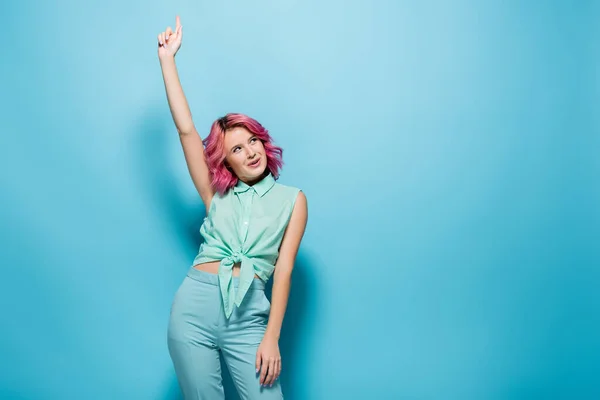 Jeune femme aux cheveux roses et main levée sur fond bleu — Photo de stock