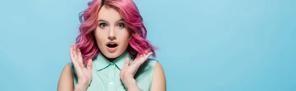 Überraschte junge Frau mit rosa Haaren und offenem Mund isoliert auf blauem, panoramischem Foto — Stockfoto
