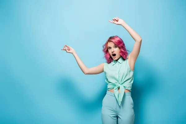 Chocado jovem mulher com cabelo rosa apontando para o lado no fundo azul — Fotografia de Stock