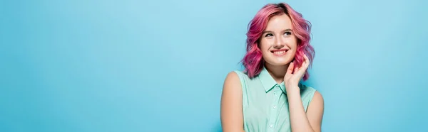 Sognante giovane donna con i capelli rosa sorridente e guardando lontano su sfondo blu, colpo panoramico — Foto stock