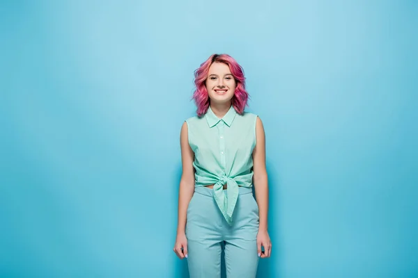 Mujer joven con el pelo rosa sonriendo sobre fondo azul - foto de stock