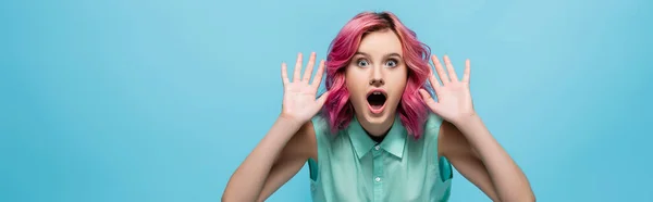 Shocked young woman with pink hair showing hands isolated on blue, panoramic shot — Stock Photo