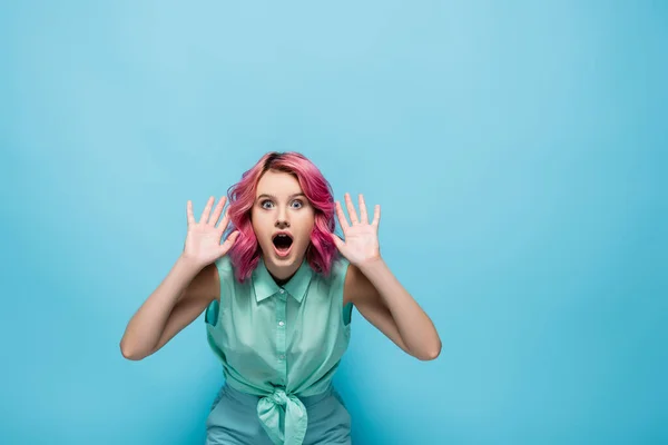 Choqué jeune femme avec les cheveux roses montrant les mains sur fond bleu — Photo de stock