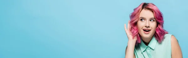 Curiosa joven con el pelo rosa escucha aislado en azul, plano panorámico - foto de stock