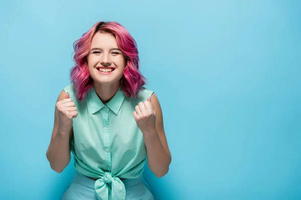 Young woman with pink hair showing yeah gesture on blue background — Stock Photo