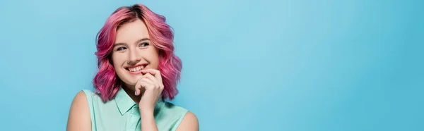 Mujer joven con el pelo rosa sonriendo y coqueteando aislado en azul, tiro panorámico - foto de stock