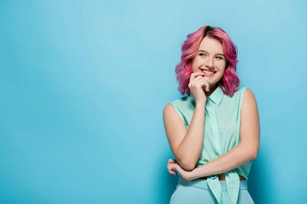Mujer joven con el pelo rosa sonriendo y coqueteando sobre fondo azul - foto de stock