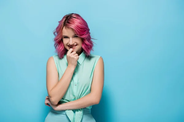 Mujer joven con el pelo rosa sonriendo y coqueteando sobre fondo azul - foto de stock