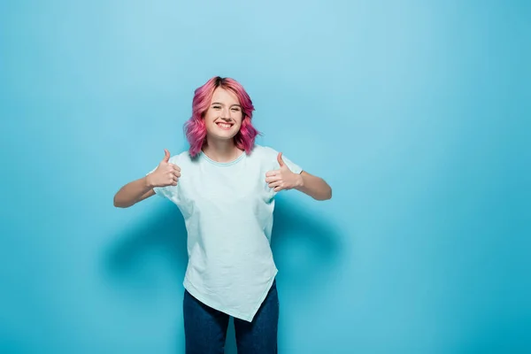 Young woman with pink hair showing thumbs up on blue background — Stock Photo