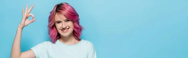 Jovem com cabelo rosa mostrando sinal ok no fundo azul, tiro panorâmico — Fotografia de Stock
