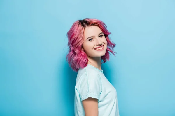 Vista lateral da jovem mulher com o cabelo rosa sorrindo no fundo azul — Fotografia de Stock