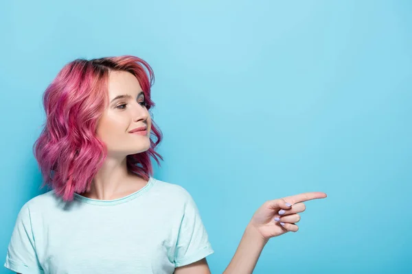 Jeune femme aux cheveux roses pointant de côté sur fond bleu — Photo de stock