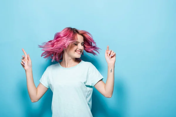 Jeune femme agitant les cheveux roses sur fond bleu — Photo de stock