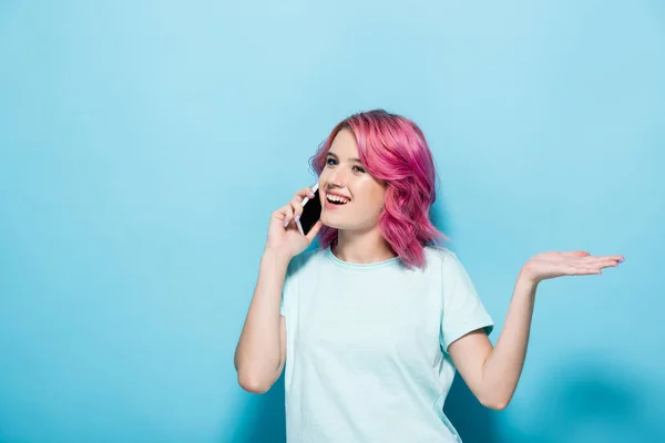 Junge Frau mit pinkfarbenen Haaren spricht auf Smartphone und gestikuliert auf blauem Hintergrund — Stockfoto