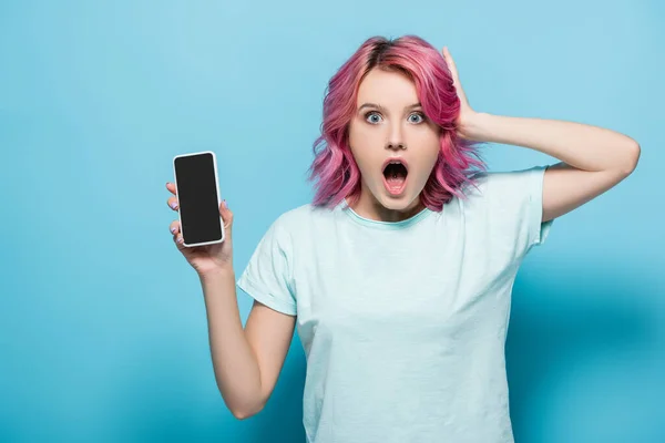 Chocado jovem mulher com cabelo rosa segurando smartphone com tela em branco no fundo azul — Fotografia de Stock