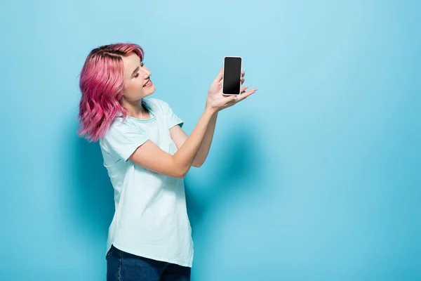 Giovane donna con capelli rosa in possesso di smartphone con schermo bianco su sfondo blu — Foto stock