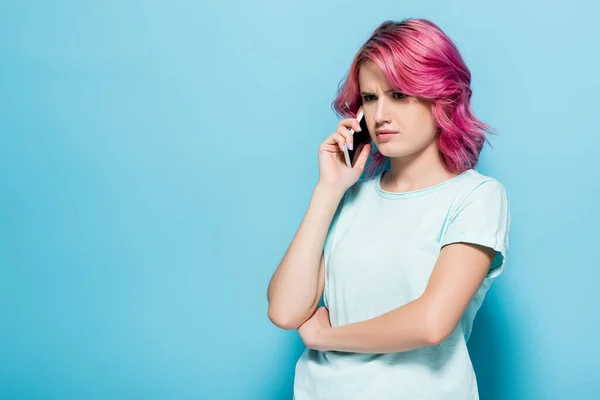 Confus jeune femme avec les cheveux roses parler sur smartphone sur fond bleu — Photo de stock