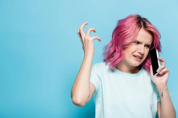 Confused young woman with pink hair talking on smartphone on blue background — Stock Photo