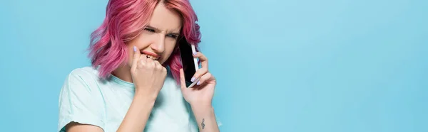 Испуганная молодая женщина с розовыми волосами разговаривает на смартфоне на синем фоне, панорамный снимок — стоковое фото