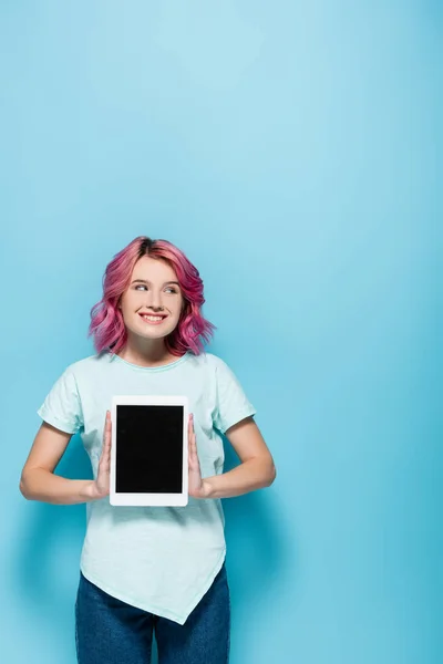 Jeune femme aux cheveux roses présentant tablette numérique avec écran blanc sur fond bleu — Photo de stock