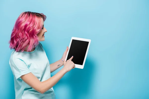 Seitenansicht einer jungen Frau mit rosa Haaren mit digitalem Tablet auf blauem Hintergrund — Stockfoto