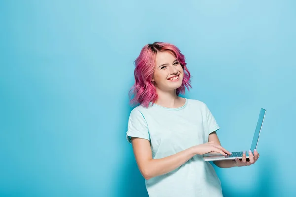 Jeune femme avec les cheveux roses en utilisant un ordinateur portable sur fond bleu — Photo de stock