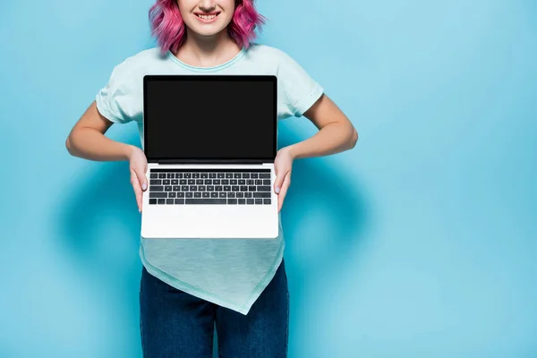 Vista recortada de la mujer joven con el pelo rosa que muestra el ordenador portátil con pantalla en blanco sobre fondo azul - foto de stock