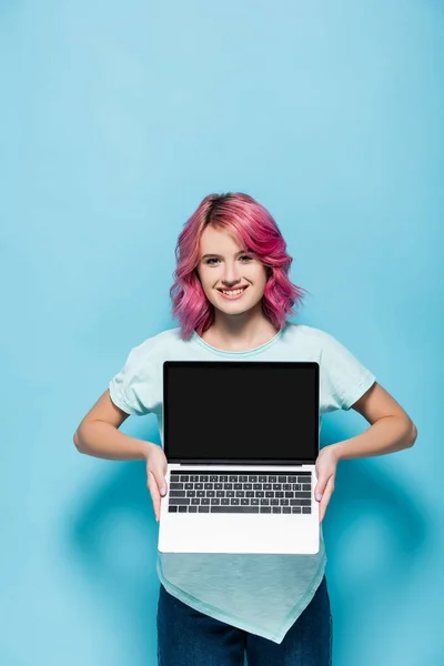 Jovem mulher com cabelo rosa mostrando laptop com tela em branco no fundo azul — Fotografia de Stock