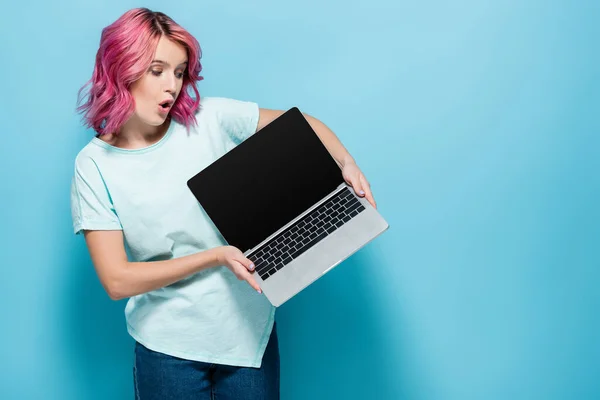 Shocked young woman with pink hair showing laptop with blank screen on blue background — Stock Photo