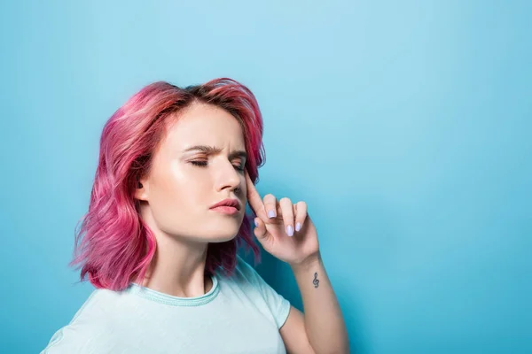 Jeune femme réfléchie avec les cheveux roses et tatouage sur fond bleu — Photo de stock