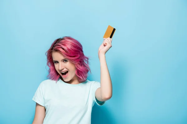 Eccitata giovane donna con capelli rosa in possesso di carta di credito su sfondo blu — Foto stock