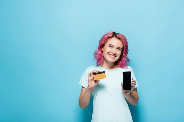 Young woman with pink hair holding credit card and smartphone on blue background — Stock Photo