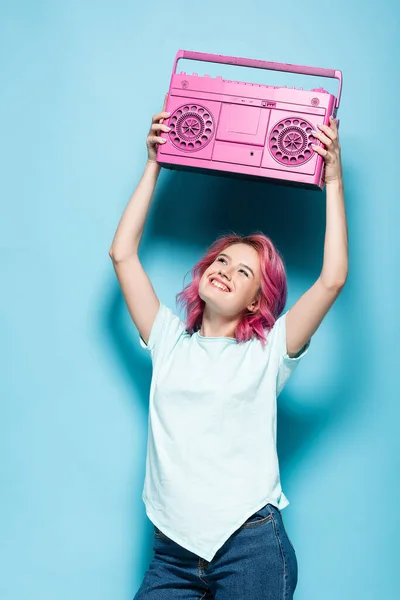 Young woman with pink hair holding vintage tape recorder on blue background — Stock Photo