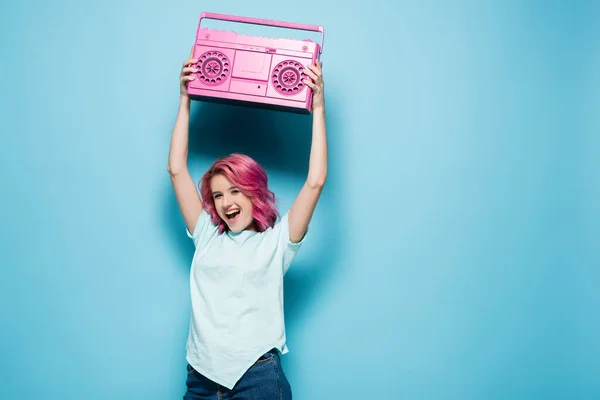 Young woman with pink hair holding vintage tape recorder on blue background — Stock Photo