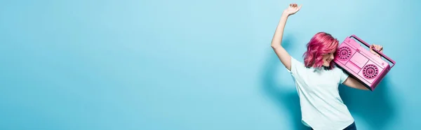 Jovem com cabelo rosa segurando gravador de fita vintage e dançando em fundo azul, tiro panorâmico — Fotografia de Stock