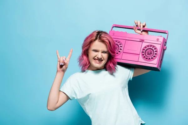 Jovem mulher com cabelo rosa segurando gravador de fita vintage e mostrando sinal de rocha no fundo azul — Fotografia de Stock