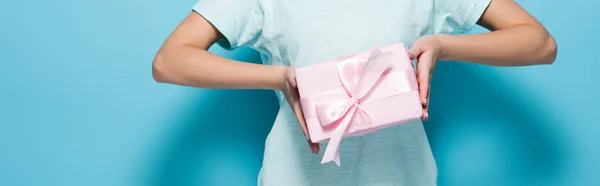 Обрезанный вид молодой женщины, держащей розовый подарочный коробок с луком на голубом фоне, панорамный снимок — стоковое фото