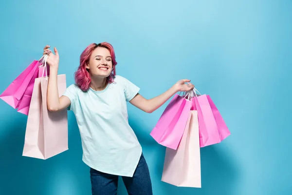 Young woman with pink hair holding shopping bags and smiling on blue background — Stock Photo