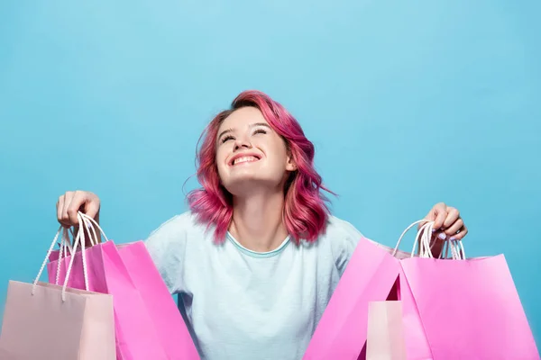 Молода жінка з рожевим волоссям тримає сумки і посміхається ізольовано на синьому — стокове фото