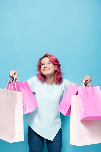 Young woman with pink hair holding shopping bags and smiling on blue background — Stock Photo