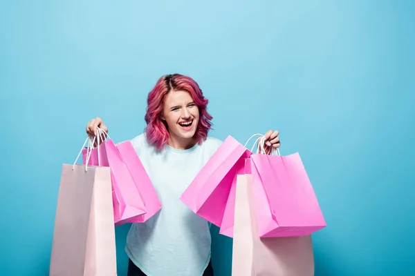 Excité jeune femme avec les cheveux roses tenant des sacs à provisions sur fond bleu — Photo de stock