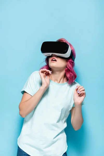 Scared young woman with pink hair in vr headset on blue background — Stock Photo